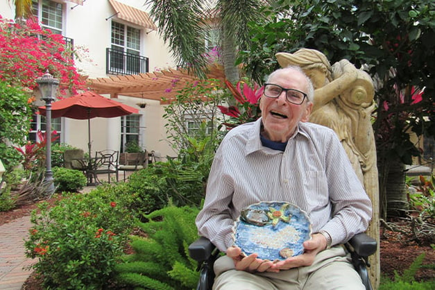 Senior man sitting in garden with painted plate in lap 
