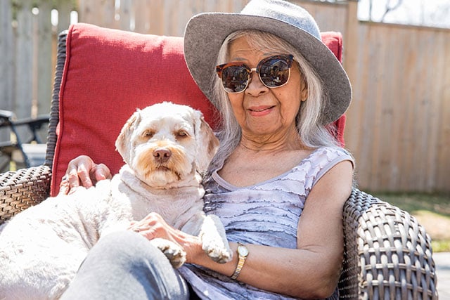 Woman wearing hat and sunglasses with white dog in her lap 